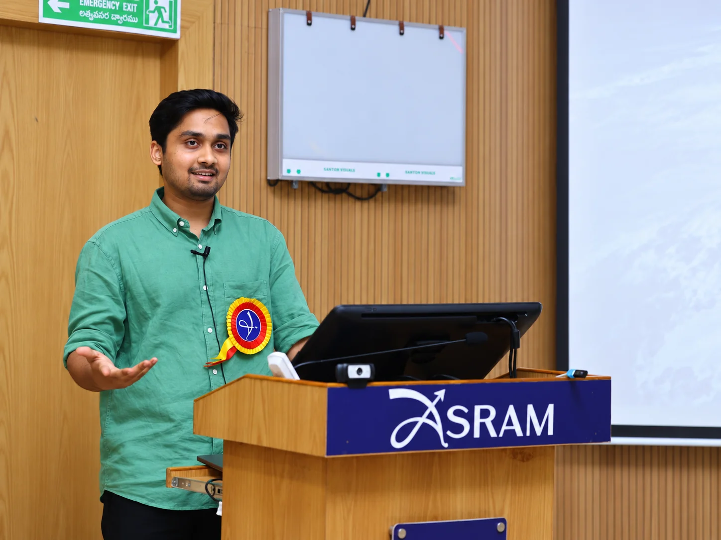 Vijay Penmetsa speaking at a lectern bearing the ASRAM name.